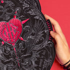 A hand displays the Doomed - Custom Initials Embroidered Patch on black fabric with detailed embroidery, set against a bright red background—ideal for those who love alternative fashion.