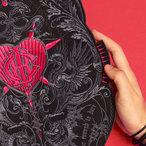 A hand displays the Doomed - Custom Initials Embroidered Patch on black fabric with detailed embroidery, set against a bright red background—ideal for those who love alternative fashion.