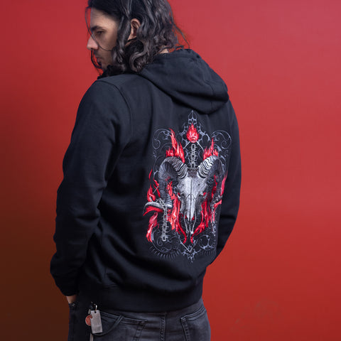 A person with long dark hair wears a black Baphomet Unisex Embroidered Hoodie featuring a large ram skull and red flames graphic on the back, standing against a solid red background for bold gothic streetwear vibes.