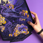 A hand holds the Crow and Peonies Embroidered Back Patch, featuring a crow with yellow and purple peonies on a purple background. The moonlit design reads "I FELL IN LOVE WITH MELANCHOLY" at the bottom.
