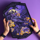 Two hands hold the Crow and Peonies Embroidered Back Patch, showing a raven among yellow and purple peonies beneath a full moon and dramatic sky. The patch is embroidered with the words: "I fell in love with melancholy.