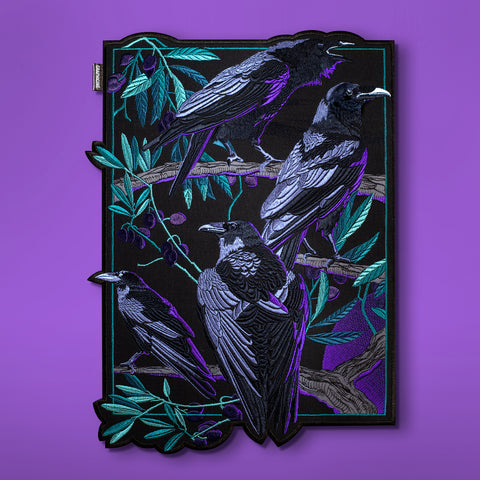 The Four Crows Embroidered Back Patch features four black crows with purple and teal accents on leafy branches against a black background, bordered by purple and set on a purple surface—a striking mystical embroidery piece.