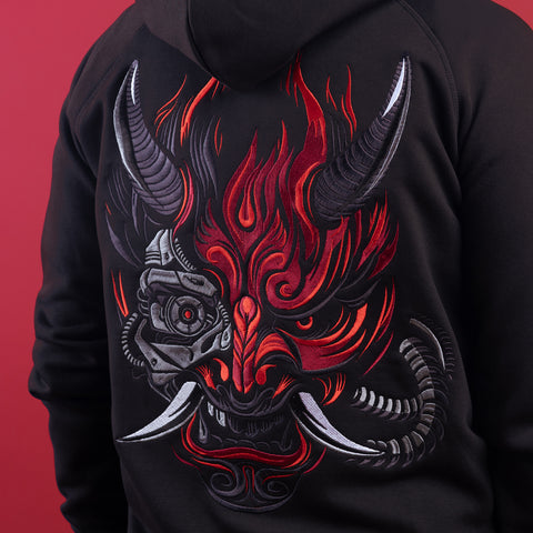 A person wearing the Cyberpunk Oni Unisex Embroidered Hoodie, flaunting a striking red, black, and gray Oni mask with half-demon, half-cybernetic features on the back—a bold embroidered design perfect for Japanese streetwear style.