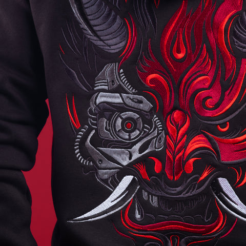Close-up of the Cyberpunk Oni Unisex Embroidered Hoodie: black hoodie with an embroidered Oni mask design, red flames, metallic accents, and white tusks, merging mechanical and demonic styles in striking Japanese streetwear.