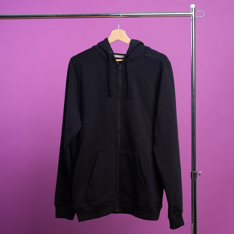 The Blesbok Unisex Embroidered Hoodie, featuring a black zip-up design with a hood and front pockets, is displayed on a wooden hanger against a plain purple backdrop, highlighting its dark pastel aesthetic.