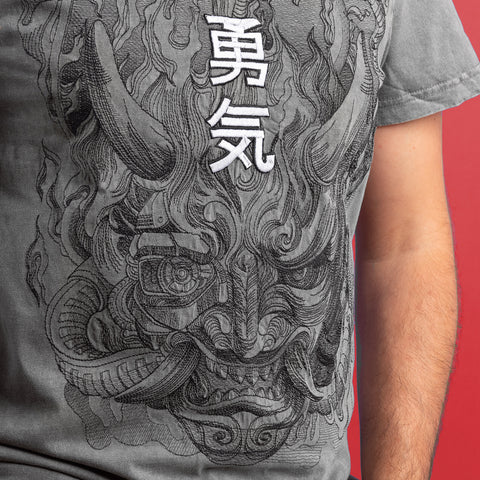 A person wears a gray Cyberpunk Oni Embroidered Unisex T-shirt, displaying a detailed horned demon face and bold white kanji above it. The red background highlights this stylish nod to Japanese mythology.