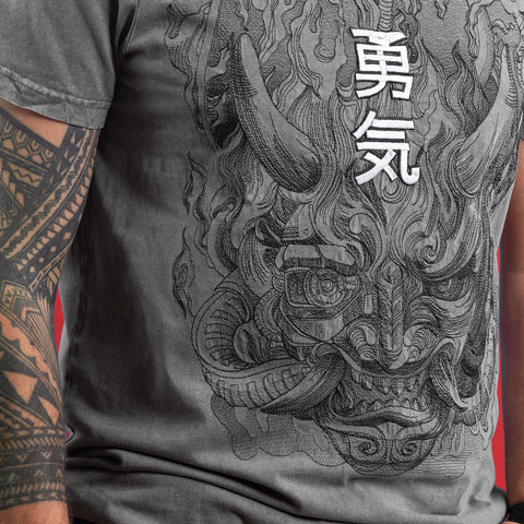 A person wears a gray Cyberpunk Oni Embroidered Unisex T-shirt with a detailed oni mask and Japanese kanji on the back, paired with a bold, geometric black tattoo inspired by Japanese mythology.