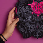 A hand displays the Doomed - Custom Initials Embroidered Patch in black and pink, featuring intricate heart, dragon, and occult designs. Set against a bold magenta background, it captures a striking alternative fashion aesthetic.