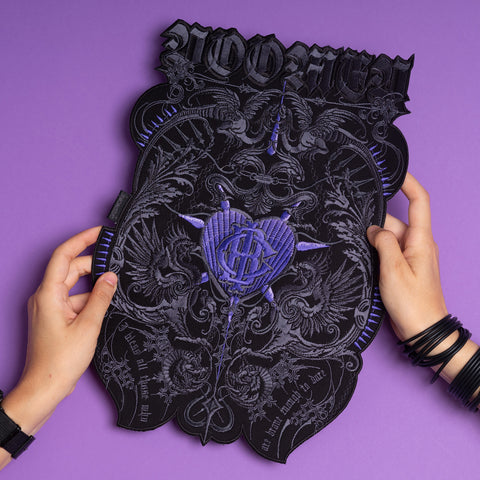 Two hands hold the Doomed - Custom Initials Embroidered Patch, featuring ornate black and purple embroidery, intricate designs, gothic lettering, and occult motifs—a bold, alternative fashion accessory shown on a purple background.