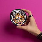 A hand with black rings and bracelets holds a Hallow Kitty Embroidered patch, featuring a fierce, roaring cat and "ROAR" text, against a bright pink background.