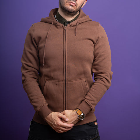 A person wearing a brown Skull Unisex Embroidered Hoodie and wristwatch stands against a purple background with hands clasped, mixing gothic streetwear with casual metal style.