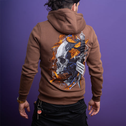 A person in a Skull Unisex Embroidered Hoodie with autumn leaves, a dagger, and "Courage Over Fear" design faces away from the camera against a purple background, embodying gothic streetwear style.