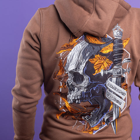 A person wears a brown Skull Unisex Embroidered Hoodie featuring a gothic skull, autumn leaves, and a sword with a "Death Before Dishonor" ribbon on the back, all set against a purple background.