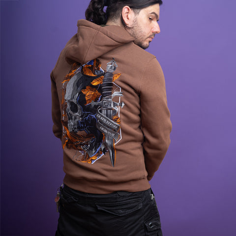 A man with long dark hair tied back wears the Skull Unisex Embroidered Hoodie, featuring a skull, dagger, orange leaves, and a Latin ribbon—ideal for gothic streetwear lovers—standing against a purple background.
