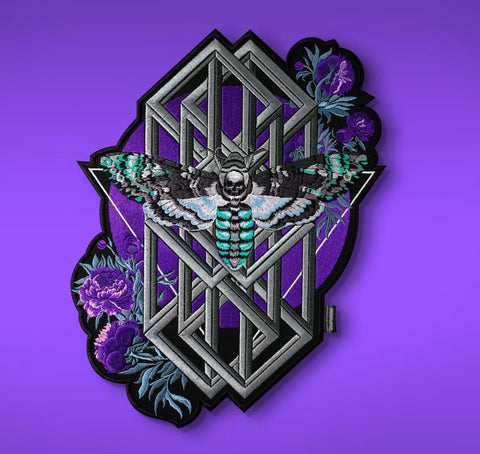 The Death’s Head Moth Embroidered Patch features a teal and black Death’s-head hawkmoth with geometric shapes and purple flowers on a vibrant purple background—ideal as an occult back patch.