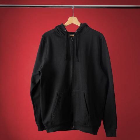 The Skull & Dagger Unisex Embroidered Hoodie, a plain black zip-up with front pockets and gothic streetwear style, hangs on a wooden hanger against a solid red background.