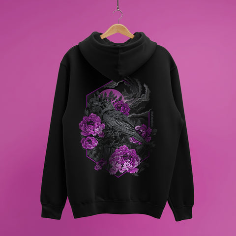 The Crow And Peonies Unisex Embroidered Hoodie, in black, hangs on a wooden hanger against a pink background, showcasing a detailed crow surrounded by purple peonies and leaves embroidered on the back.
