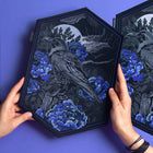 A person holds the Crow & Peonies Goth Embroidered Patch, featuring a crow with blue flowers and a moonlit night sky on a hexagonal black canvas with a purple background.