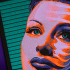 The Vaporware Synth Pop Embroidered Back Patch features a stylized woman’s face in purple, orange, and pink with green eyes and long lashes on a teal-striped background atop a purple gradient surface.