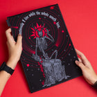 A person holds the Vicarious Embroidered Back Patch, featuring a skeleton on a tree stump, red rings, and "I live while the whole world dies" on a solid red background—ideal for fans of occult fashion.