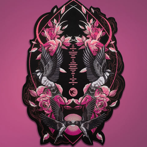 The Spotify Song Code Embroidered Patch features a symmetrical design with black and white birds, pink roses, and leafy vines on a black background, framed by a bold outline and shown on a pink surface for a striking, customizable look.