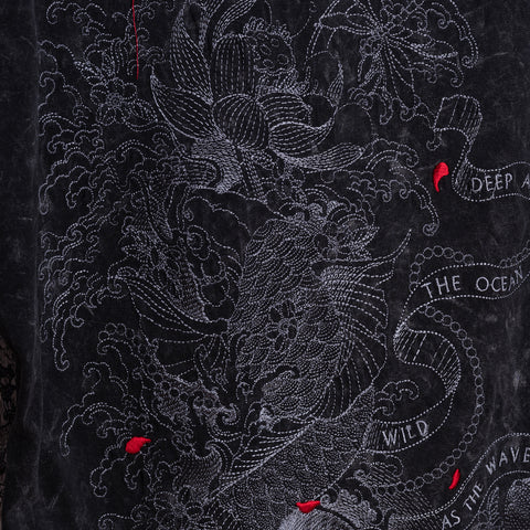 The Japanese Koi Fish Embroidered Female T-shirt features white embroidery of a koi, flowers, and red accents on dark acid-wash cotton. Curved text reads “DEEP AS THE OCEAN, WILD AS THE WAVES.”.