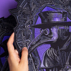 A hand holds the Plague Doctor Embroidered Back Patch, showcasing a gothic plague doctor with a beaked mask and wide-brimmed hat on a purple-accented background—perfect for Victorian cosplay.