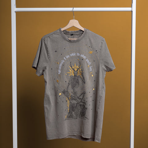 The Vicarious Embroidered Unisex T-shirt, in gray, hangs on a wooden hanger. It showcases a crowned skeleton with a sword, gold accents, gothic style, and the text "We cannot live a true while the whole world lies" on a mustard yellow background.